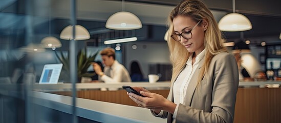 Young Caucasian female designer going over paperwork while using a smartphone in a startup company office. Copyspace image. Header for website template - obrazy, fototapety, plakaty
