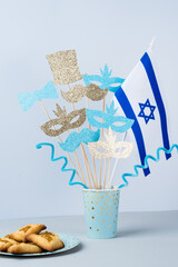 Purim celebration concept. Masks, bow, hat, mustached on a stick with the Jewish flag. Festive pastries hamans ears
