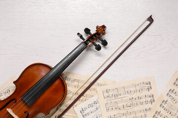 Fototapeta premium Violin, bow and music sheets on white wooden table, top view