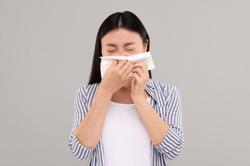 Suffering from allergy. Young woman with tissue sneezing on grey background