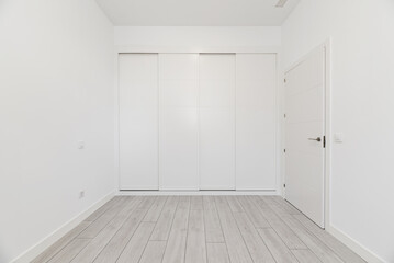 An empty room in a loft-type home with a built-in wardrobe covering the entire wall with white wooden sliding doors