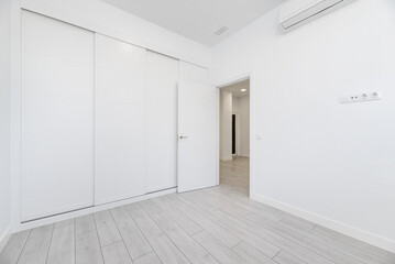 An empty room in a loft-type home with a built-in wardrobe that covers the entire wall with white...