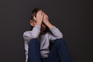 Child abuse. Upset boy near gray wall