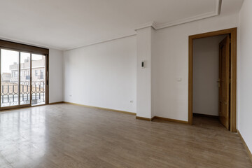 Empty living room with dusty wooden floors and a French window with a balcony and sliding glass and...