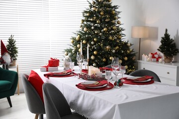 Christmas table setting with burning candles, gift box and dishware in room