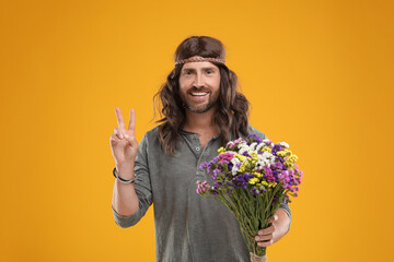 Hippie man with bouquet of colorful flowers showing V-sign on orange background