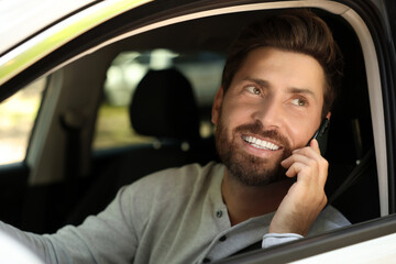 Happy bearded man talking on smartphone in car, view from outside