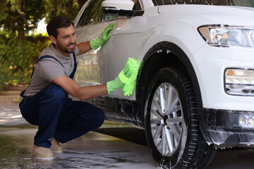 Worker washing auto with sponge at outdoor car wash