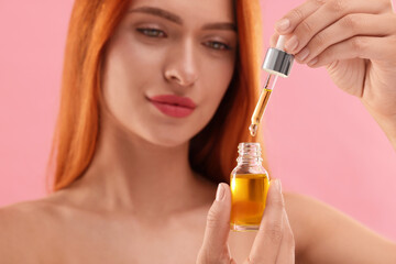 Fototapeta premium Beautiful young woman with bottle of serum on pink background, selective focus