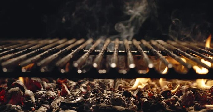 Against dark background, coal burns bright red. Rare tongues of flame escape from hot coal making their way through grill grate. Delicious aromas are in air in anticipation of mouth-watering treat. AD