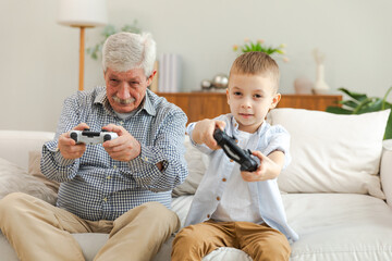 Happy family. Old senior man grandfather boy grandson playing video game with joysticks at home. Smiling grandparent and child using gamepads for video game. Older generation modern tech usage