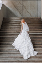 Fototapeta na wymiar A beautiful bride in a white lace long dress stands on stone steps outdoors. Wedding photography, portrait.