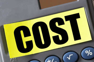 COST word on a yellow piece of paper placed on a calculator. Concept for business.