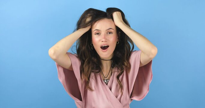 Happy woman looking camera shocked surprised say wow put hands on face, touch her hair. Wow, it is awesome. Surprised girl face. Close up of shocked woman face expression isolated on blue background