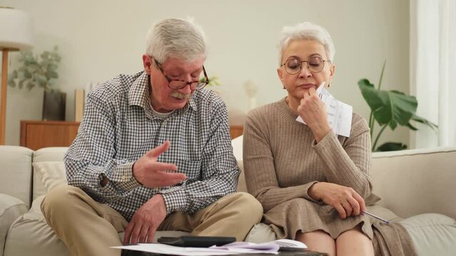 Middle aged senior couple sit with paper document doing financial paperwork. Older mature man woman reading paper bill managing bank finances calculating taxes planning loan debt pension payment