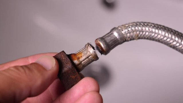 Plumber close-up holds used broken hose all rusty and on neck of flexible hose, full of plaque due to fact that there is lot of lime in water