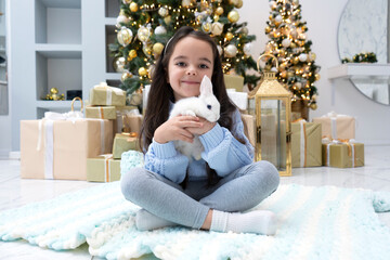 Little cute girl with white rabbit pet waiting holidays and 2024 New Year Eve. Magical Christmas time. A rabbit is a symbol of the outgoing 2023 year.