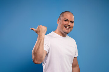 man pointing to the side with the thumb of his right hand, smiling