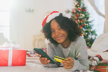 African American woman shopping online holding smartphone paying with gold credit card for...