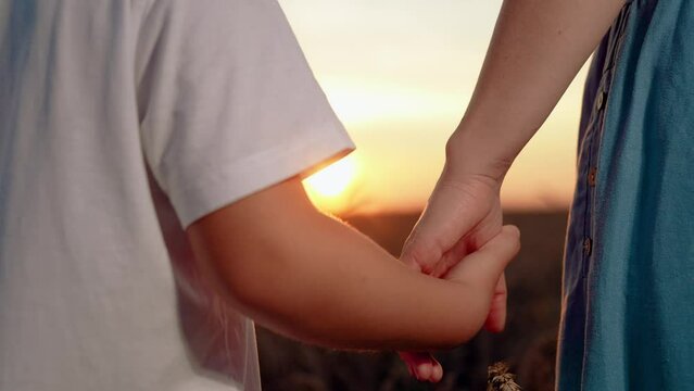 Closeup mother lets go of child hand, separation. Separation of hands of mother and son. Family at sunset. Child and mother share hands in front of sun. Separation, parting, quarrel. Misunderstanding