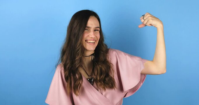 Feminism and women power. Do it! Self assured proud woman brags about her strength raises arm and shows muscles in hands. Girl show her power and look proud. I am strong and independent stand on blue.