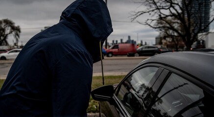 Fototapeta na wymiar A car thief is breaking into a car in broad daylight in Toronto, Ontario, Canada.