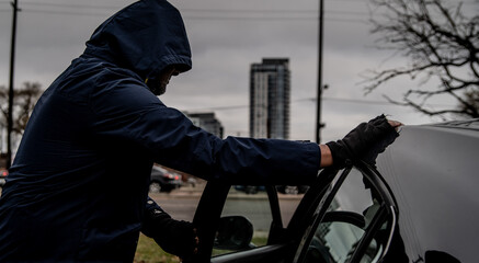 A car thief is breaking into a car in broad daylight in Toronto, Ontario, Canada.