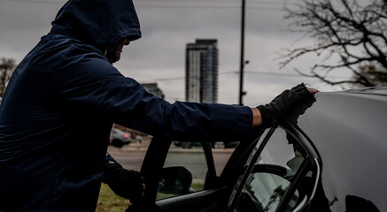 A car thief is breaking into a car in broad daylight in Toronto, Ontario, Canada.