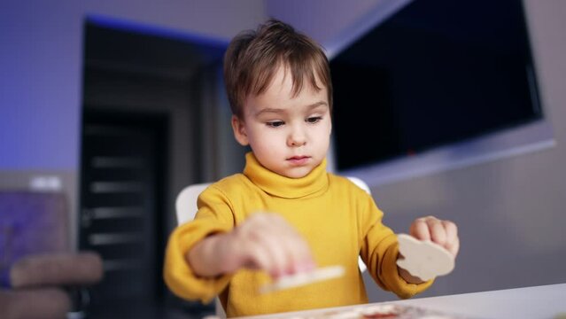 Beautiful Caucasian toddler is busy with a game. Calm baby boy focused on collecting puzzles. Close up. Blurred backdrop.