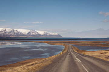 road leading along coast of lake to volcanic mountains. High rocky peaks covered with snow layer...