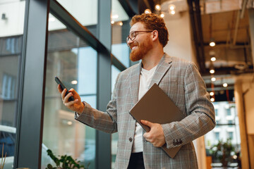 Handsome sales manager with laptop standing on modern coworking background and use phone