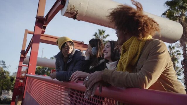 Multicultural group laughing people meeting leaning on railing outdoors. Joyful young friends enjoying together winter free day. Social positive relationships in college students of Generation z.