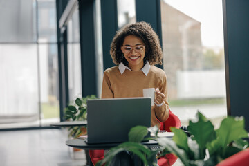 Smiling female freelancer have coffee break during working on laptop in modern coworking