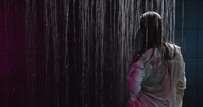 Sexy wet woman under shower in neon light enjoying water flows, moving erotically. Provocative woman
