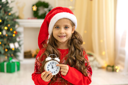 Little girl baby child holding white alarm clock. New Year's clock at midnight. Twelve O'clock midnight in retro style. Christmas decoration on wood background. a clock displays just before New Year