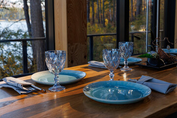 Preparing for party in forest luxury restaurant on river bank. Decorated served table await guests. Decoration Details. large window with wild mountain forest view. Tourism and vacations