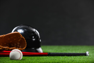 Baseball bat, batting helmet, leather glove and ball on green grass against dark background. Space...