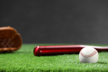 Baseball bat and ball on green grass against dark background. Space for text
