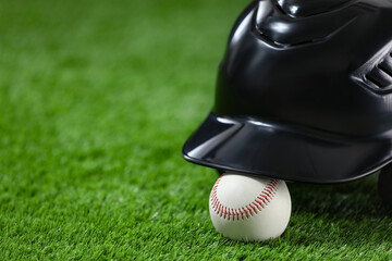 Batting helmet and baseball ball on green grass, closeup. Space for text