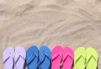 Many stylish colorful flip flops on sand outdoors, flat lay. Space for text