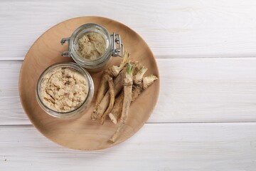 Platter with tasty prepared horseradish and roots on white wooden table, top view. Space for text