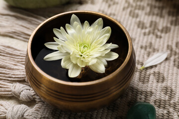 Tibetan singing bowl with water and beautiful chrysanthemum flower on table, closeup
