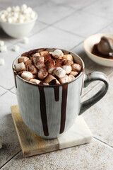 Delicious hot chocolate with marshmallows and cocoa powder in cup on tiled table