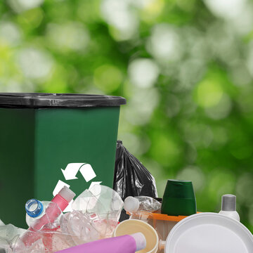 Waste bin surrounded by garbage on blurred background, space for text