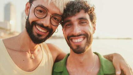 Close-up of gay couple standing embracing and looking at the camera with smile