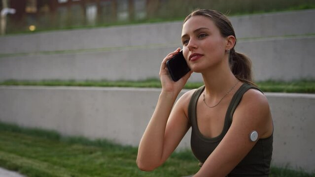 Diabetic woman sitting outdoors, having a call outside in the city park.