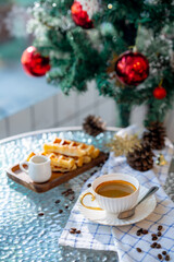 Obraz na płótnie Canvas Cup of hot coffee and bakery goods Various waffles and breads are on the table. and decorated with Christmas There is a Christmas tree and various decorations. to celebrate the Christmas festival.