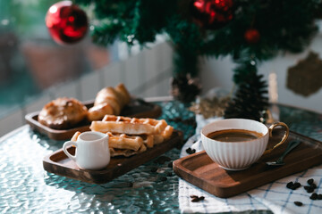 Cup of hot coffee and bakery goods Various waffles and breads are on the table. and decorated with Christmas There is a Christmas tree and various decorations. to celebrate the Christmas festival.