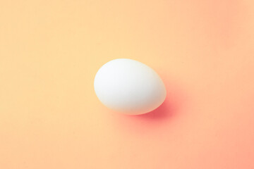 One white chicken egg on an peach background. Preparing for Happy Easter. Food photo. Empty egg for...