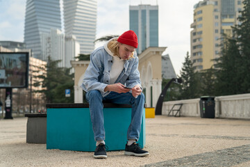 Pensive hipster man sitting in urban street with smartphone, reading, messaging, searching...